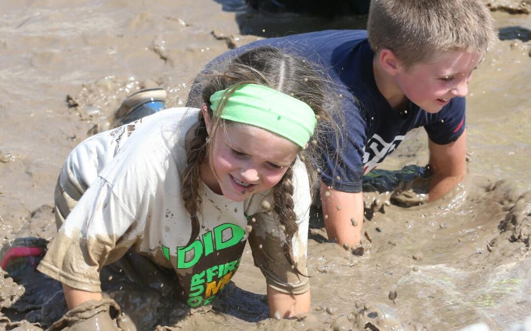 a little girl and a boy playing in the mud