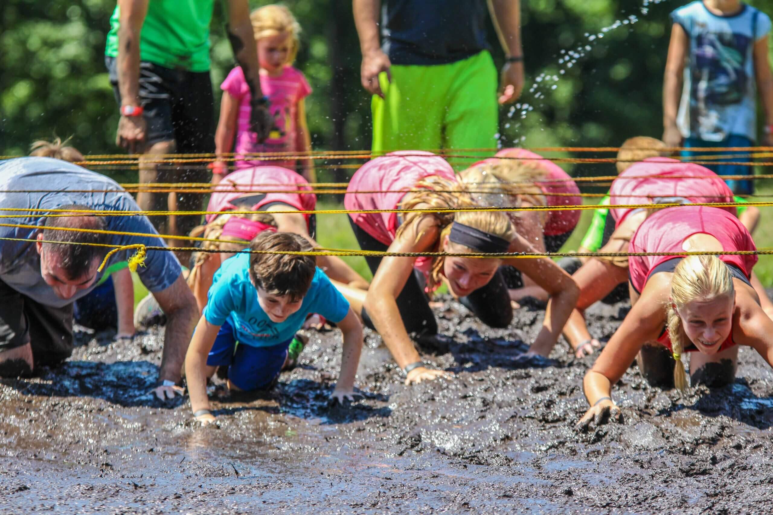 adults and kids are crossing the ropes in a mud run