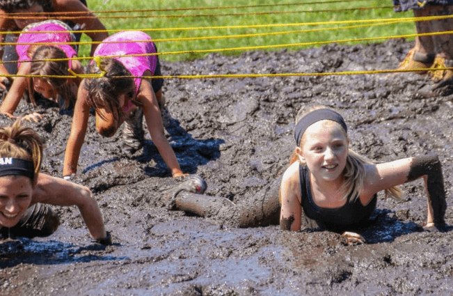 a little girl in a black top enjoying the mud run